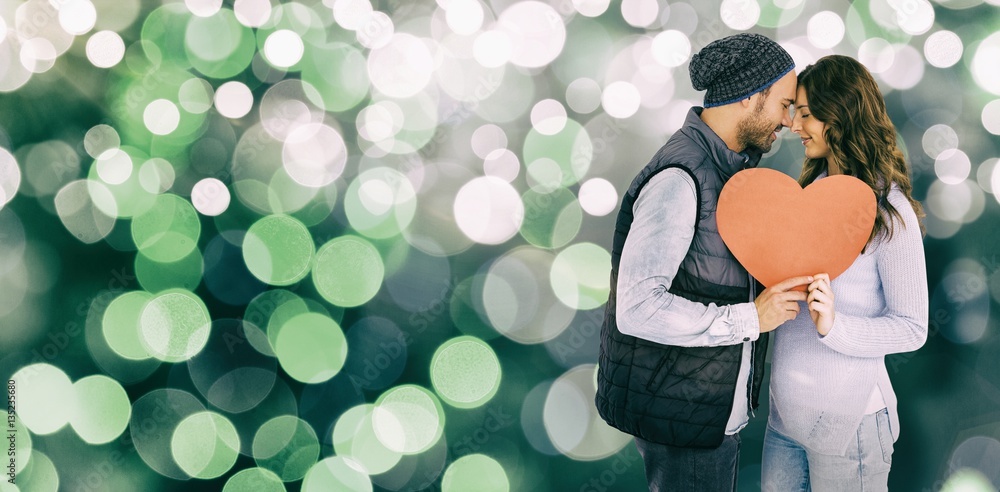 Composite image of happy young couple holding heart shape paper