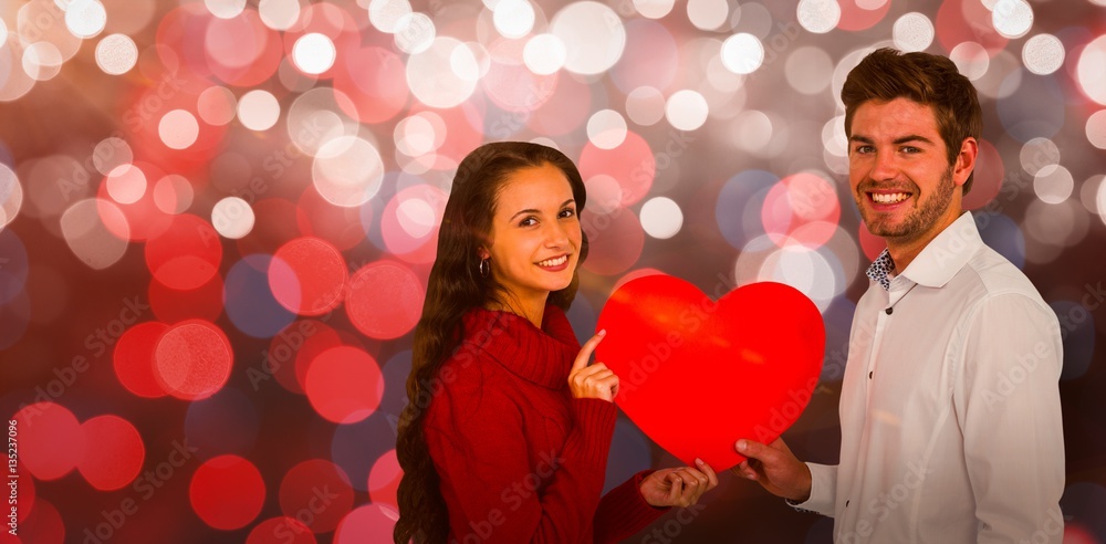 Composite image of smiling couple holding paper heart