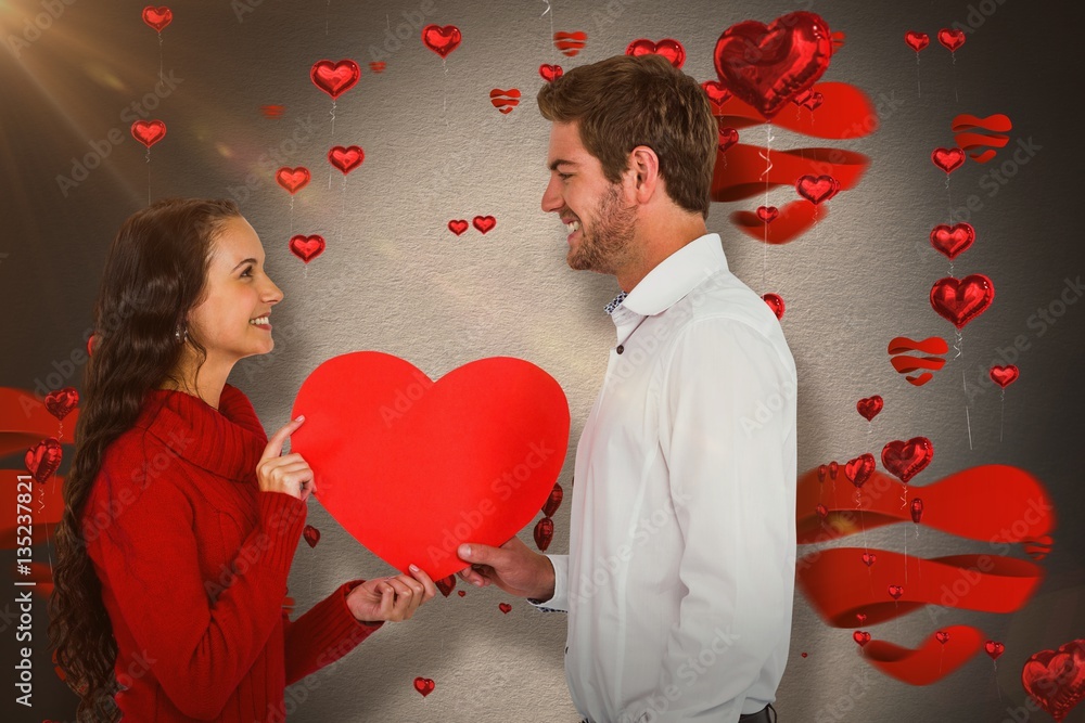 Composite image of smiling couple holding paper heart