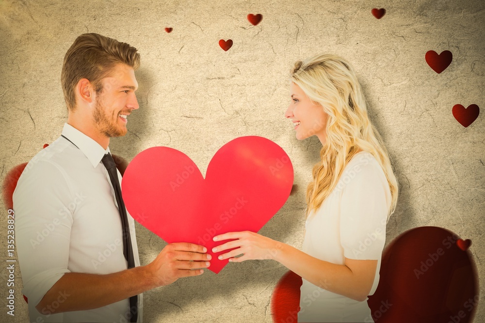 Composite image of attractive young couple holding red heart