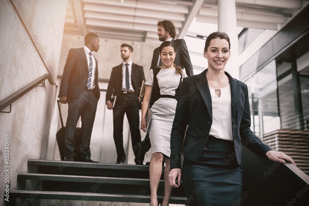 Confident businesswoman with colleagues climbing down stairs