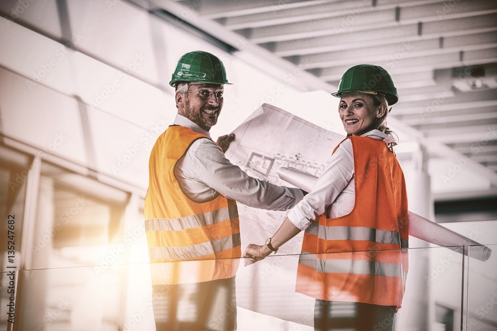 Architects holding blueprint while standing in office