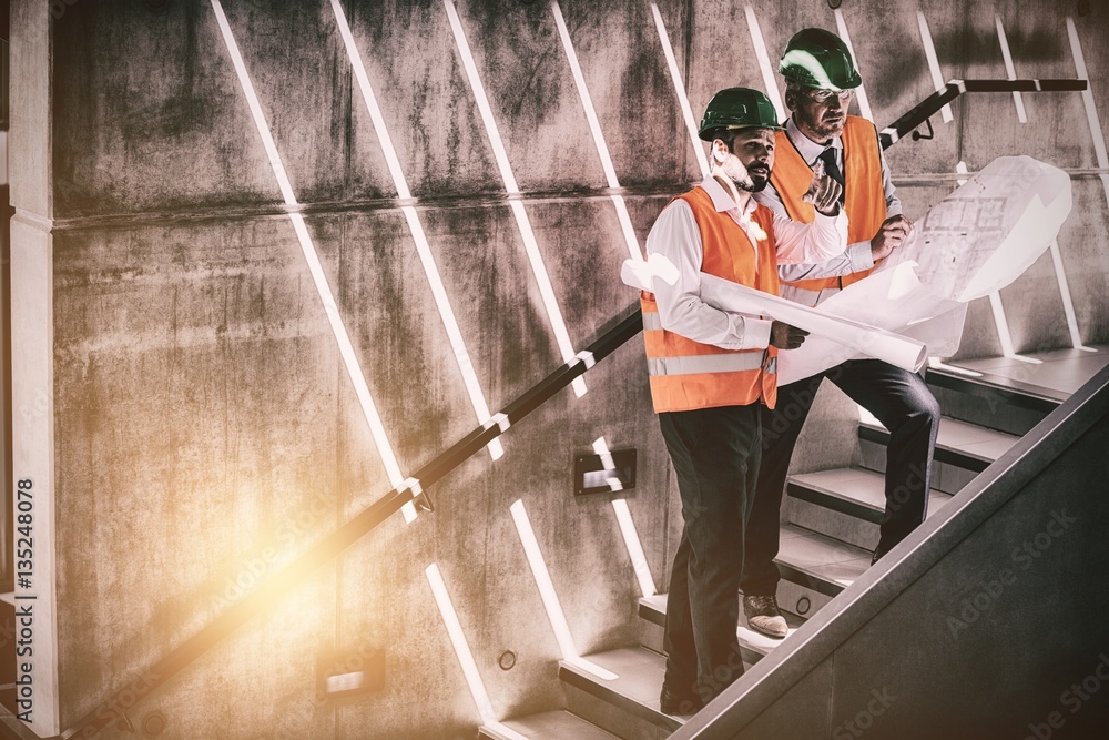 Architects standing on staircase discussing with blueprint