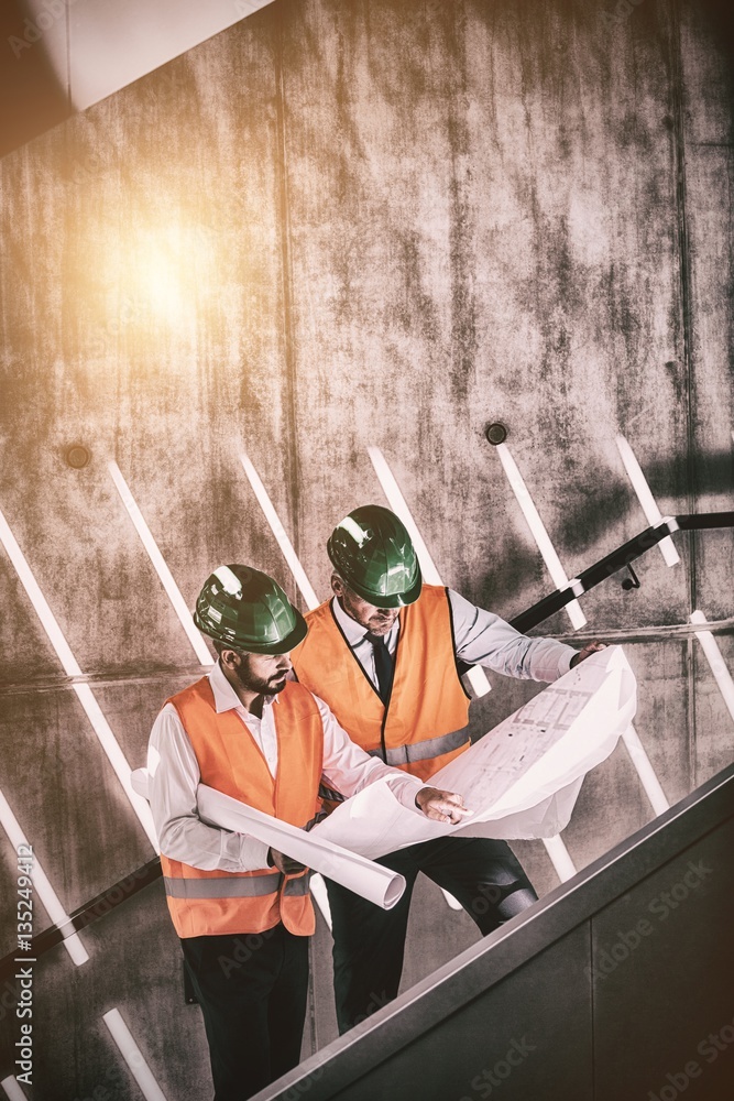 Architects standing on staircase discussing with blueprint