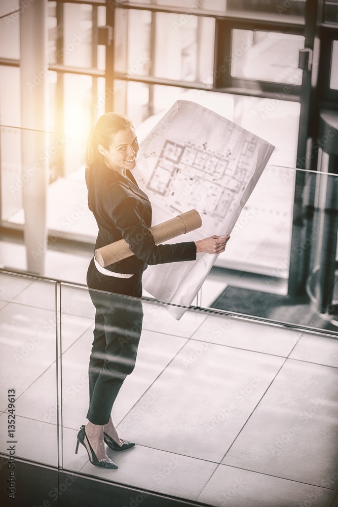 Businesswoman standing at office corridor with blueprint