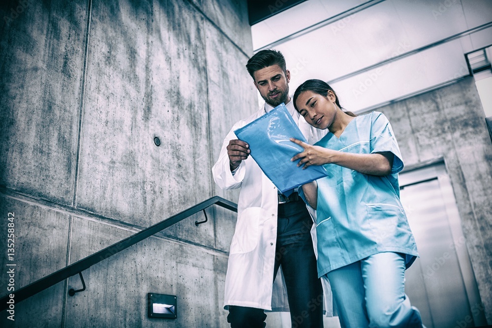 Doctor and nurse looking at report while climbing down stairs