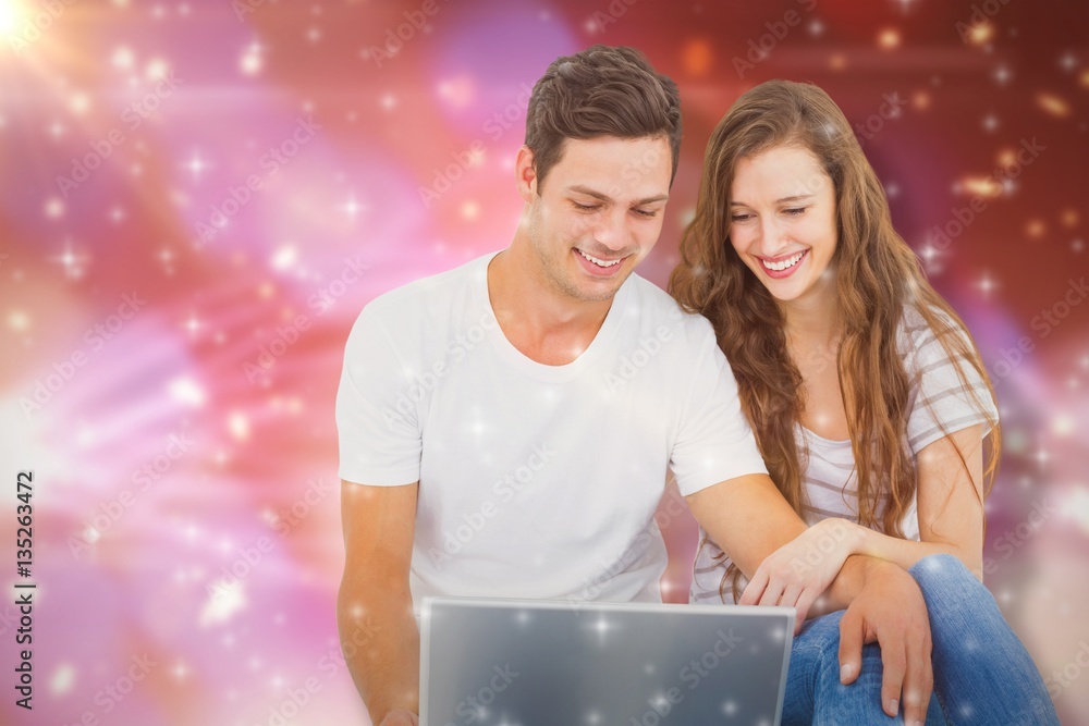 Composite image of young couple sitting on floor using laptop