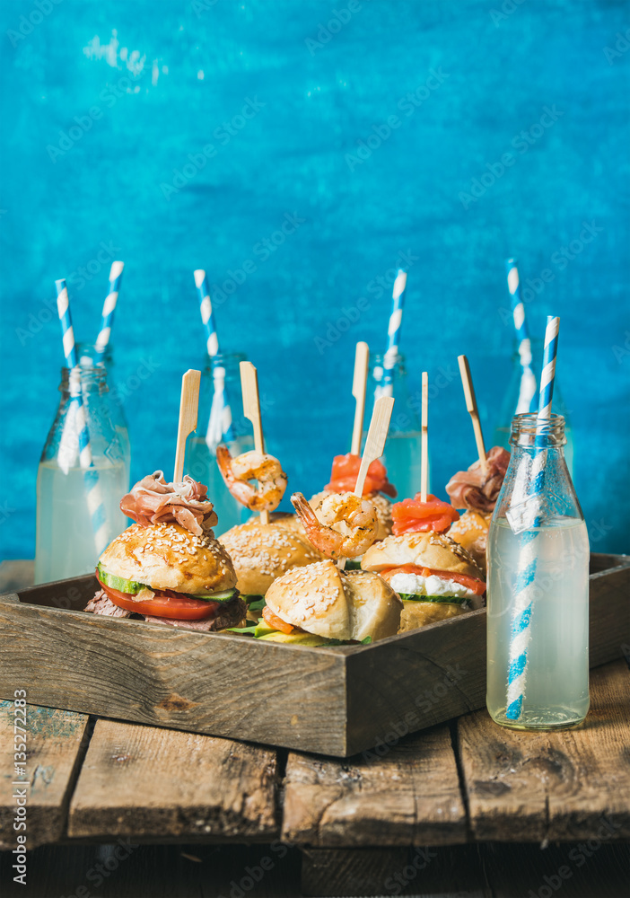 Home party food concept. Homemade burgers with sticks in wooden tray and lemonade in bottles with st