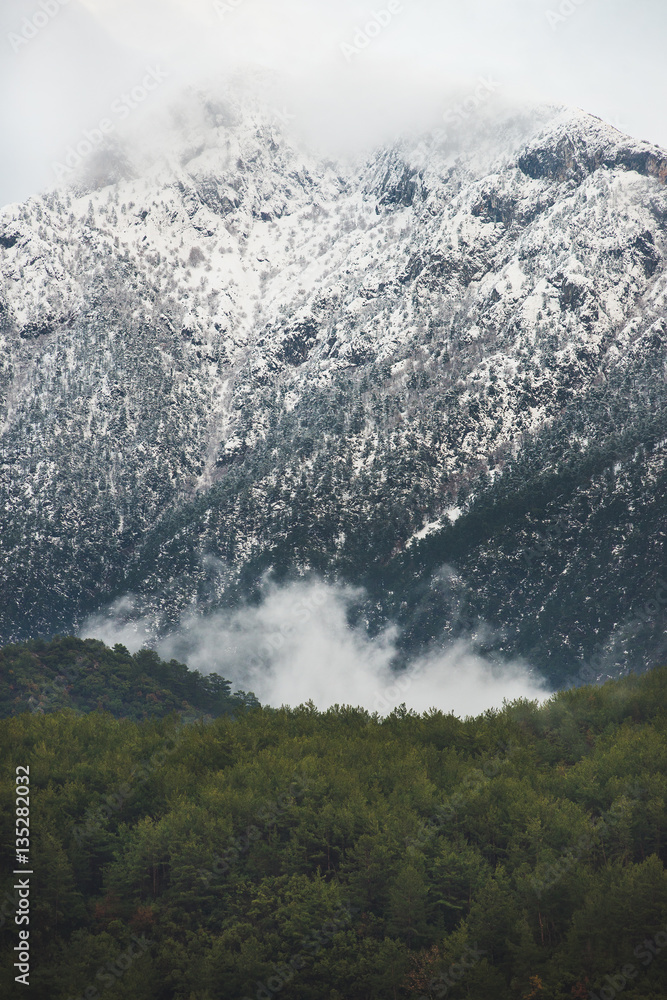 Green slopes of the Taurus mountains covered with snow and clouds in winter on gloomy day. Southern 