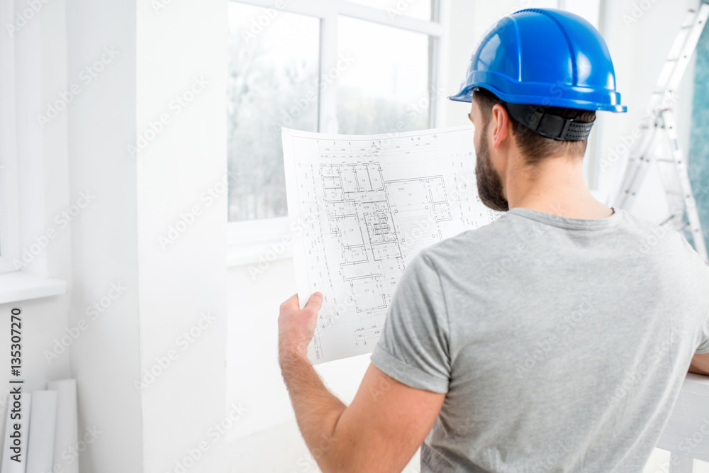 Handsome repairman or builder in helmet working with drawings on renovation of interior