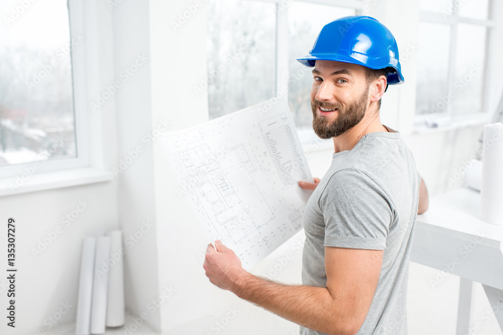 Handsome repairman or builder in helmet working with drawings on renovation of interior