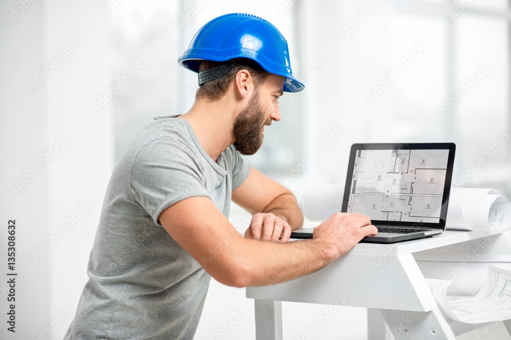 Handsome architect or foreman in helmet working with laptop on the apartment drawings at the structu