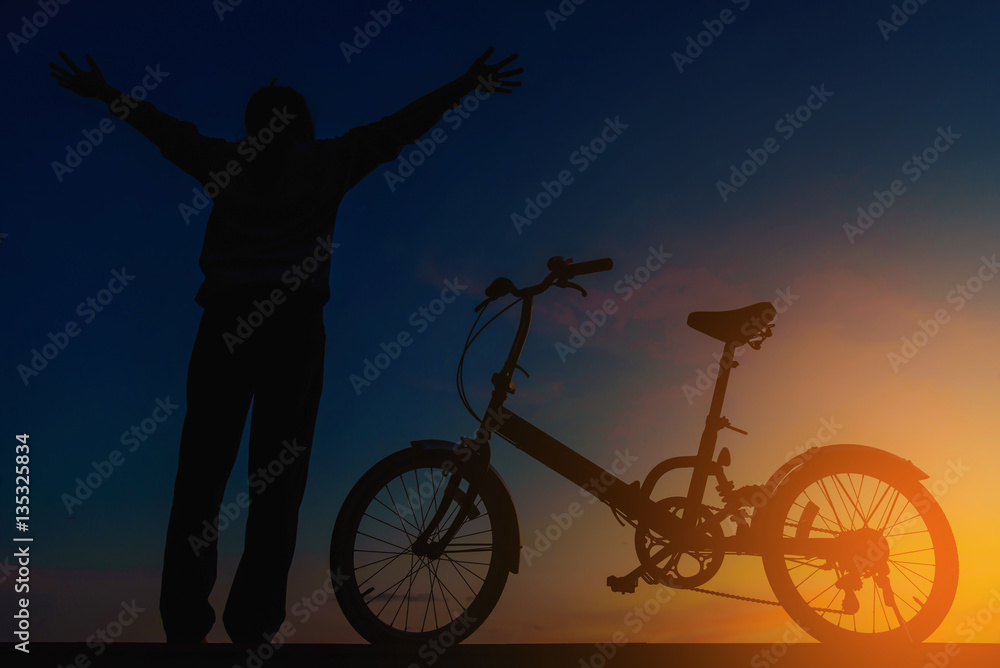 Silhouette woman and bicycle on dramatic sky at sunset.