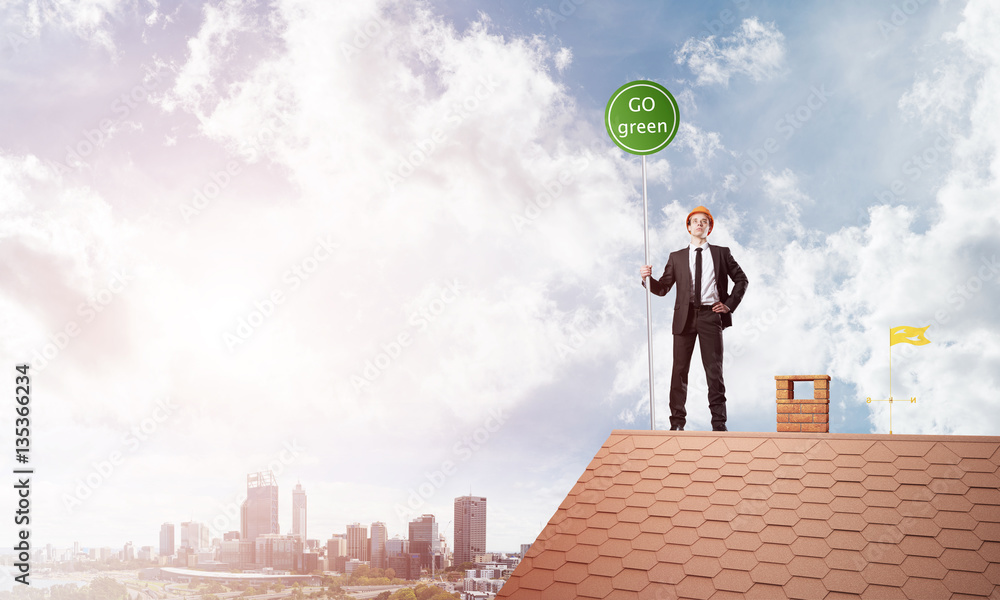 Businessman in suit on house top with ecology concept signboard. Mixed media