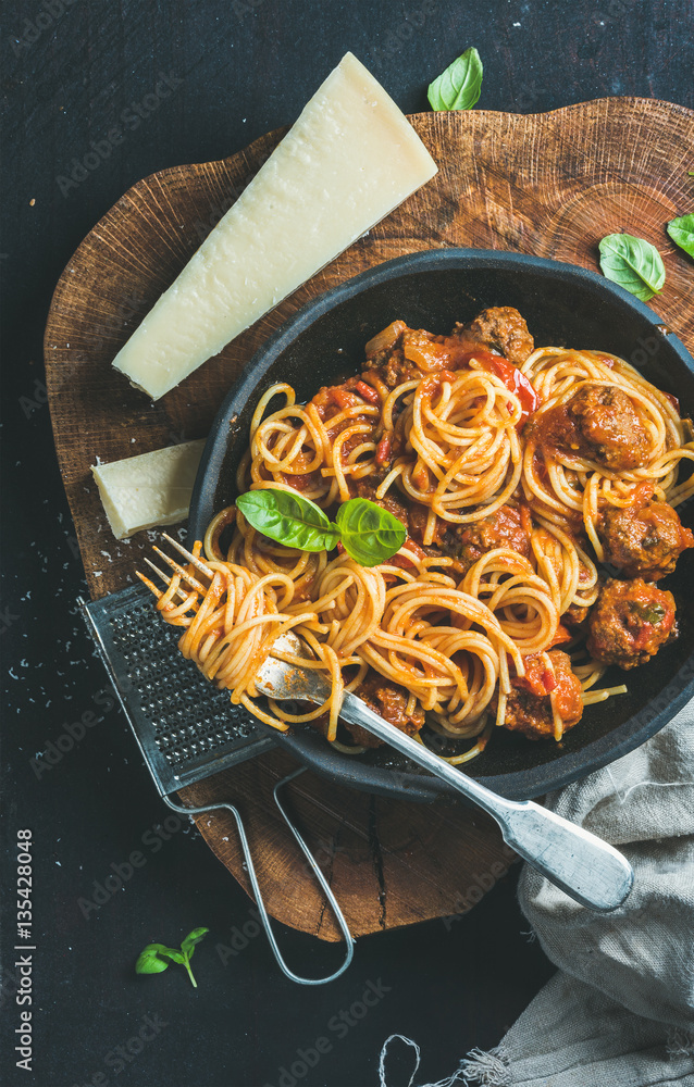 Italian pasta dinner. Spaghetti with meatballas, basil and parmesan cheese in black plate over dark 