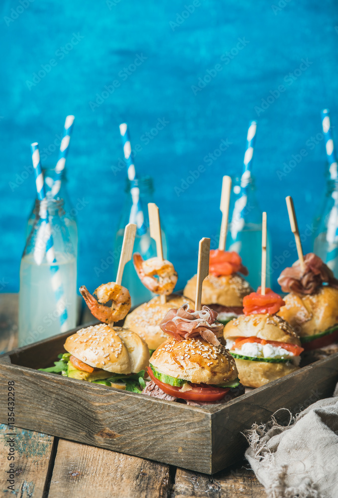 Home party food concept. Homemade burgers in wooden tray and lemonade in glass bottles with straws o