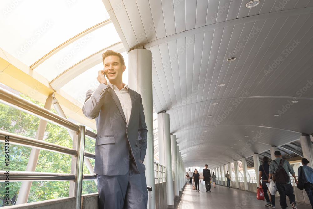 Business man talking via smart phone on the walk way with people