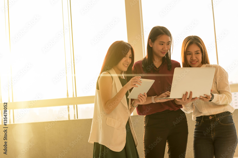 Three woman use laptop together in afternoon sun