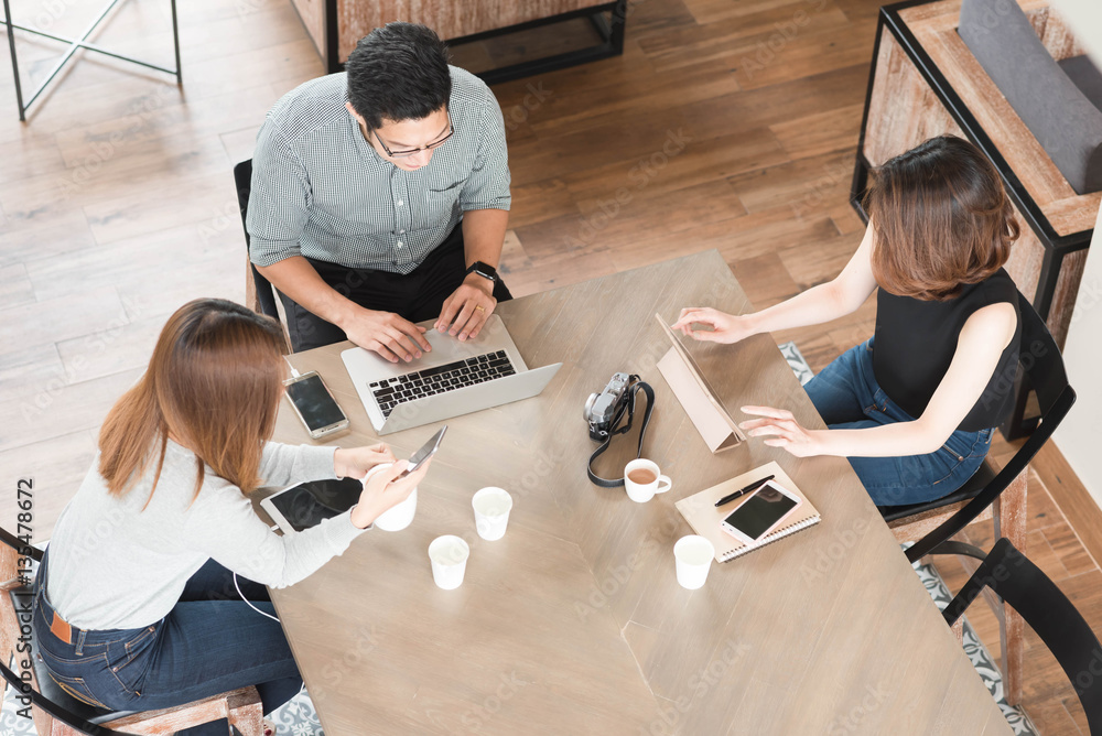 Group of three friends meeting in coffee shop, using smartphone