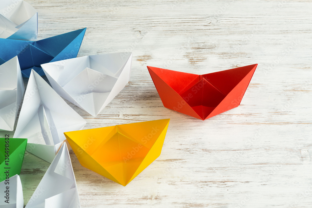 Business leadership concept with white and color paper boats on wooden table