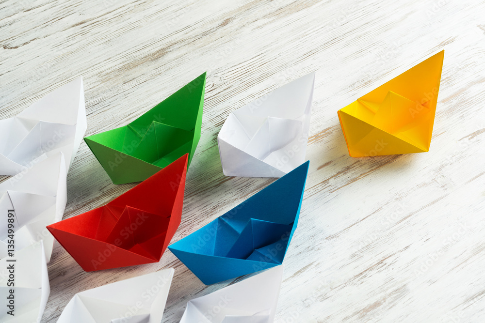 Business leadership concept with white and color paper boats on wooden table