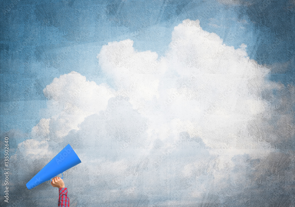 Hand of woman holding paper trumpet against blue concrete background