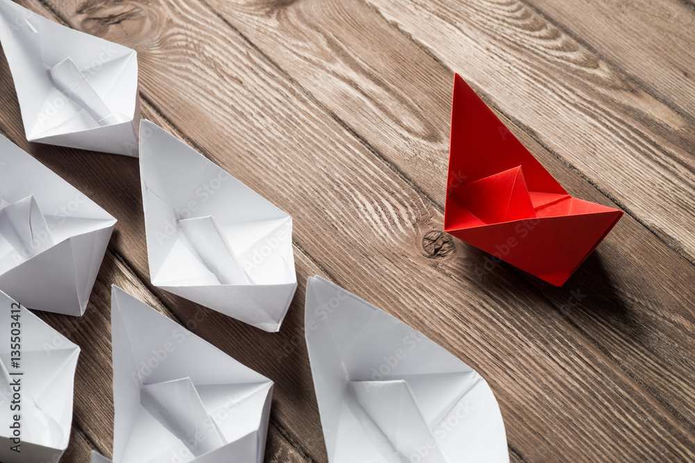 Business leadership concept with white and color paper boats on wooden table