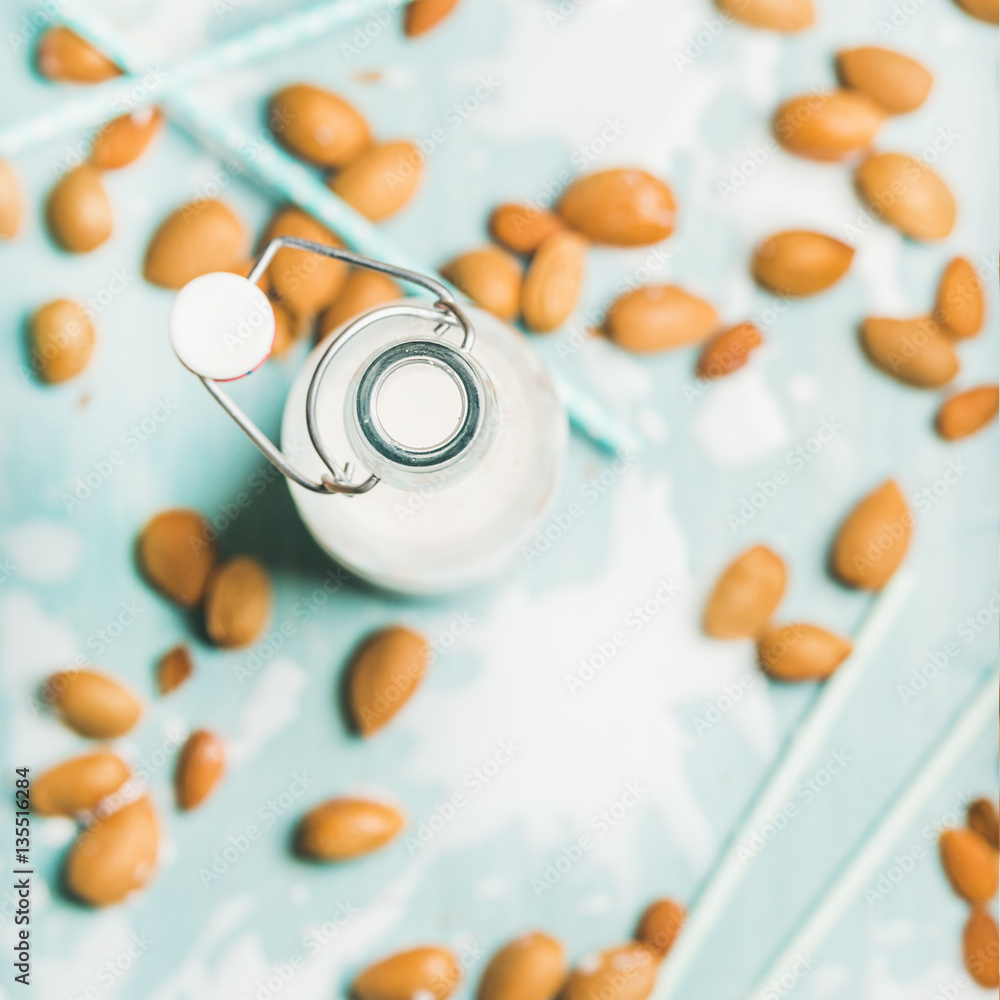 Dairy alternative milk. Almond milk in bottle and fresh nuts over blue background, top view, selecti