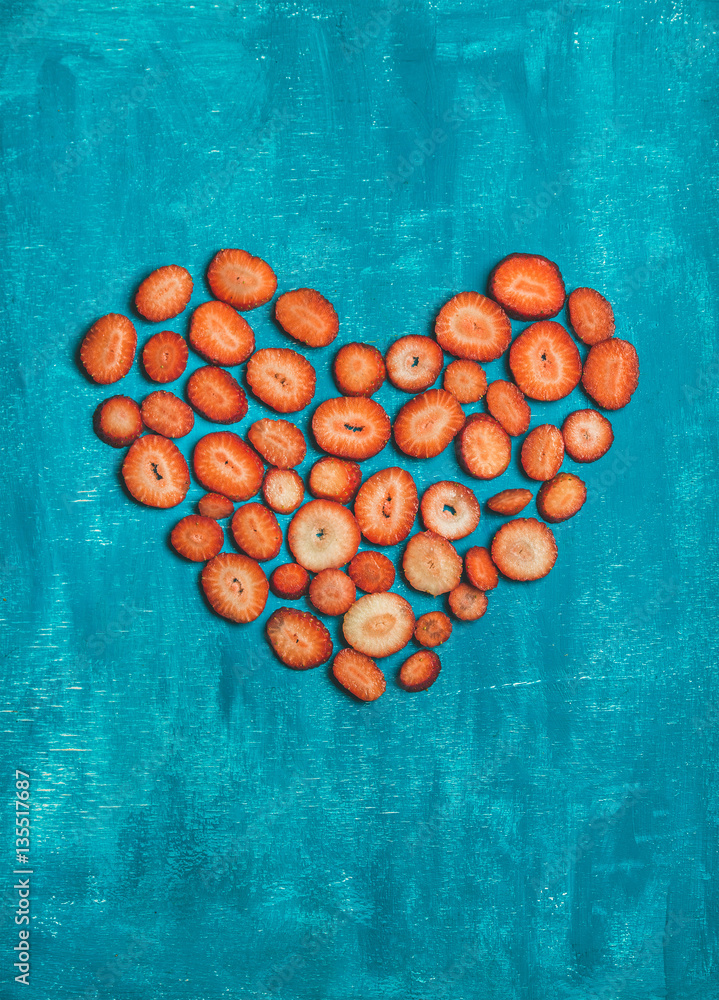 Pieces of fresh red strawberry placed in shape of heart over bright blue painted wooden background, 