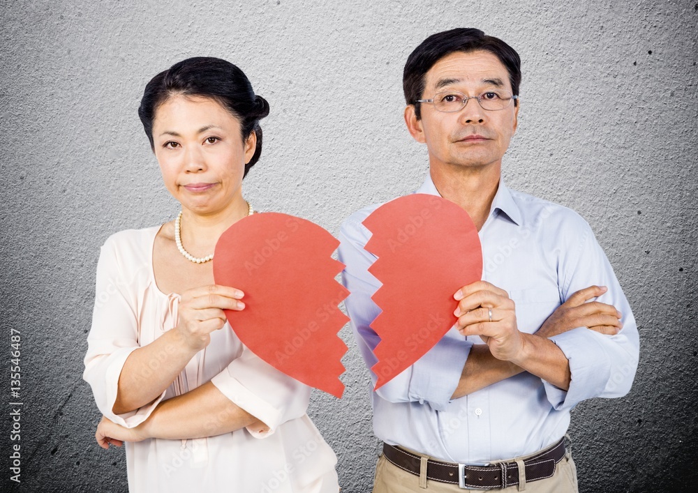 Displeased mature couple holding broken heart