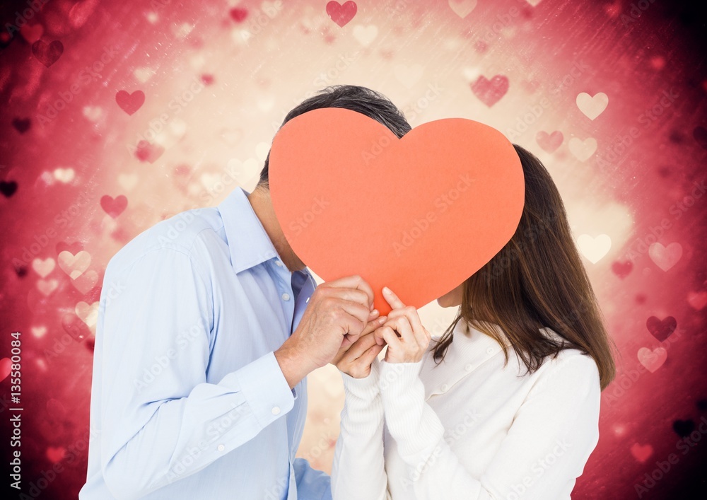 Romantic couple hiding their face behind heart