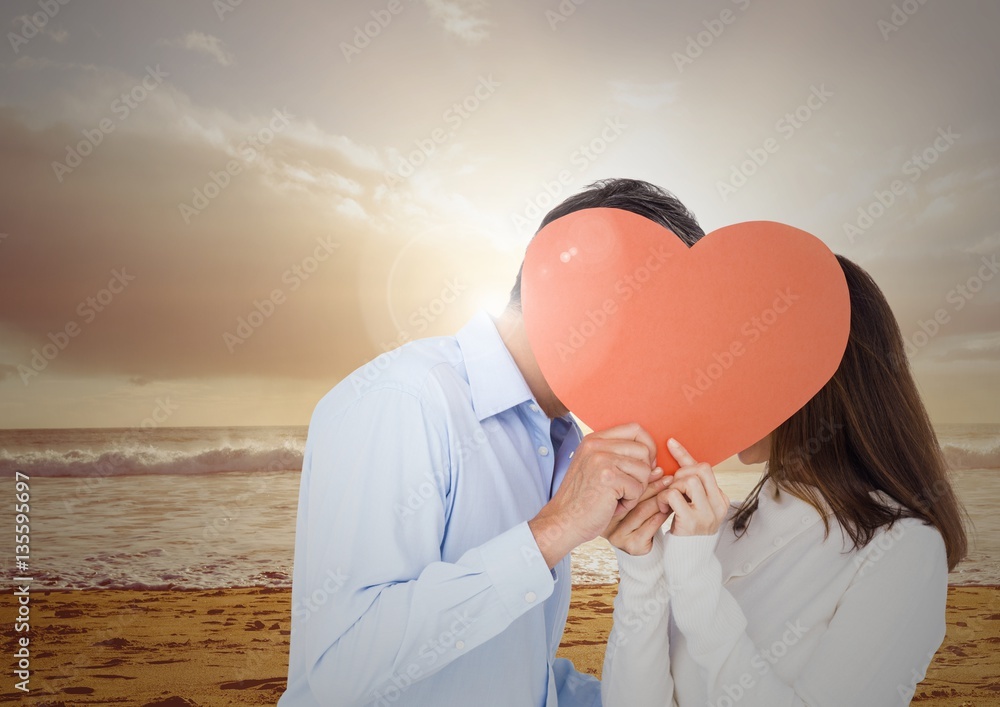 Romantic couple hiding their face behind red heart