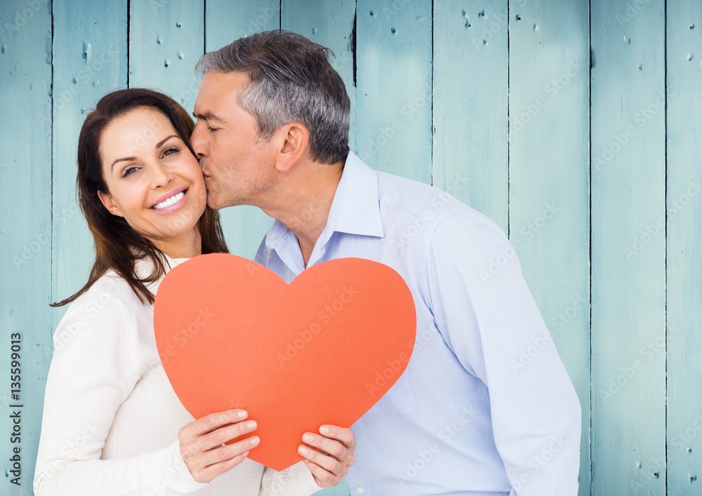 Mature man kissing a woman holding red heart