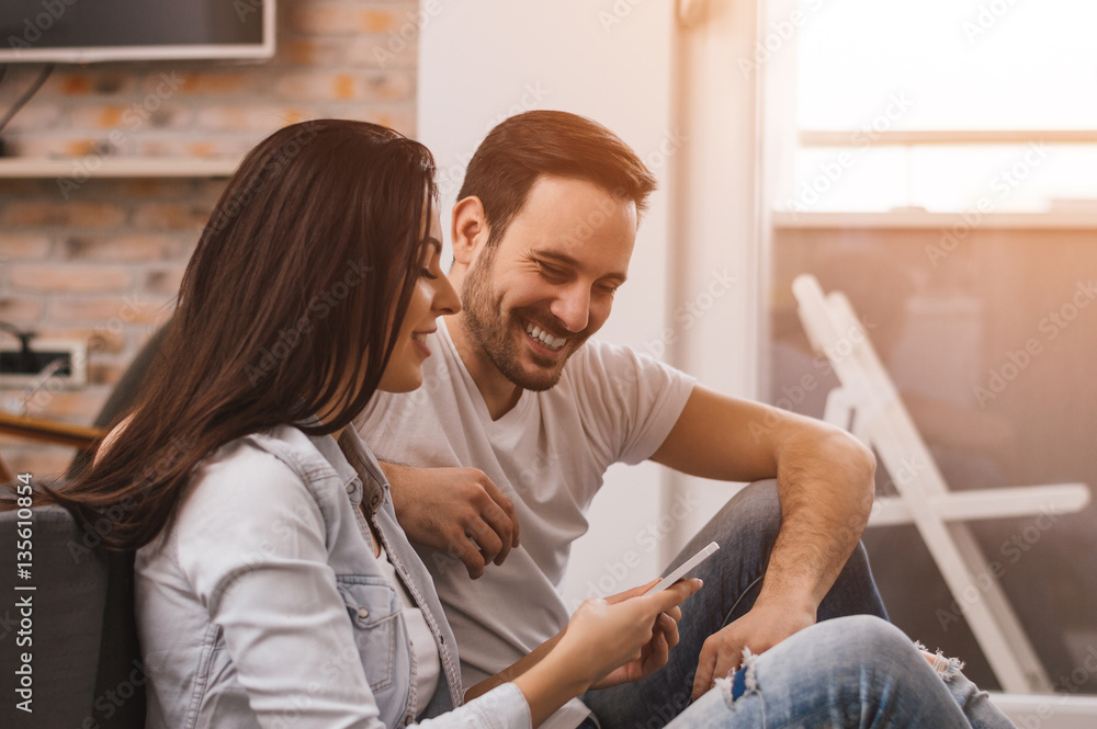 Happy couple enjoying media content in a smart phone sitting on