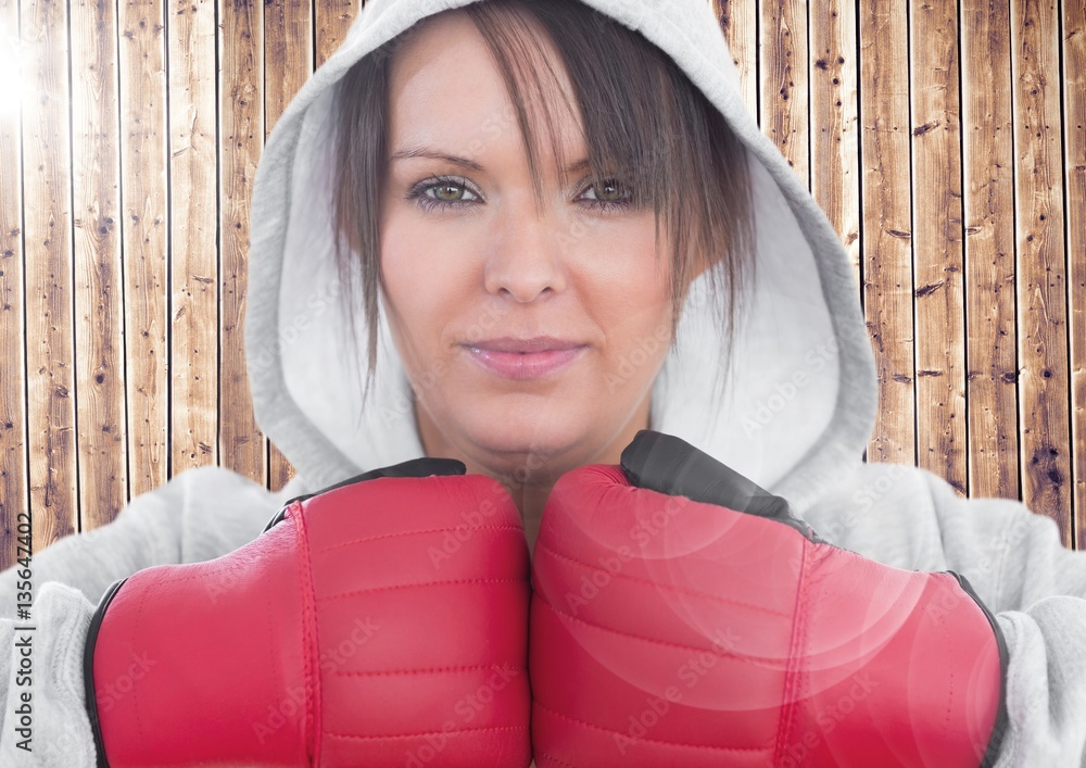 Woman in boxing gloves standing against wooden background