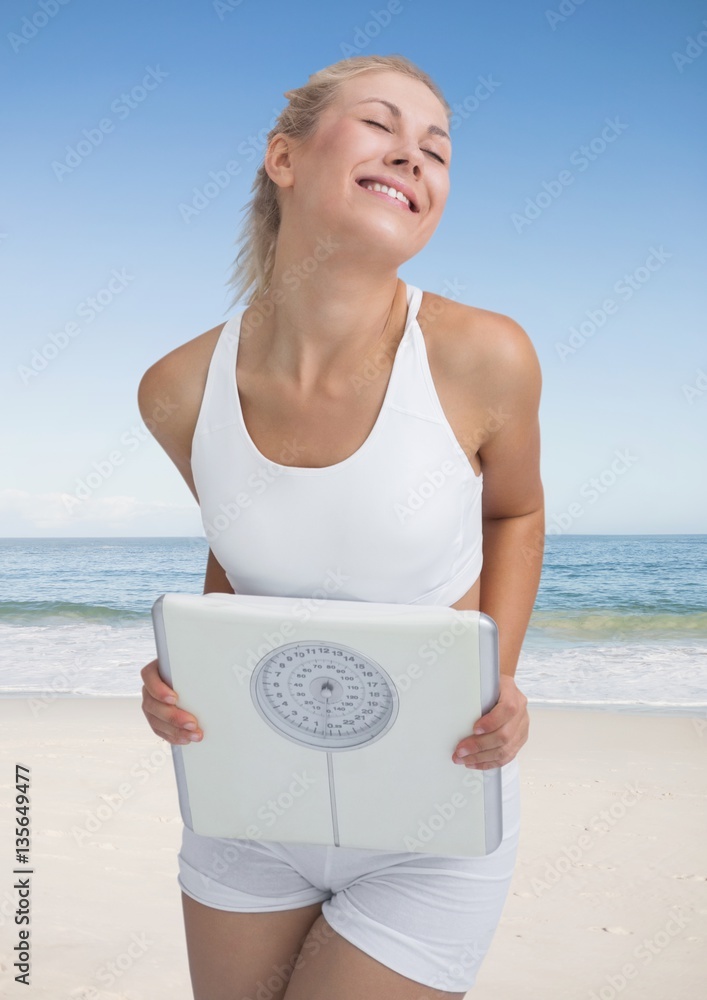 Fit woman holding a weight scale on the beach