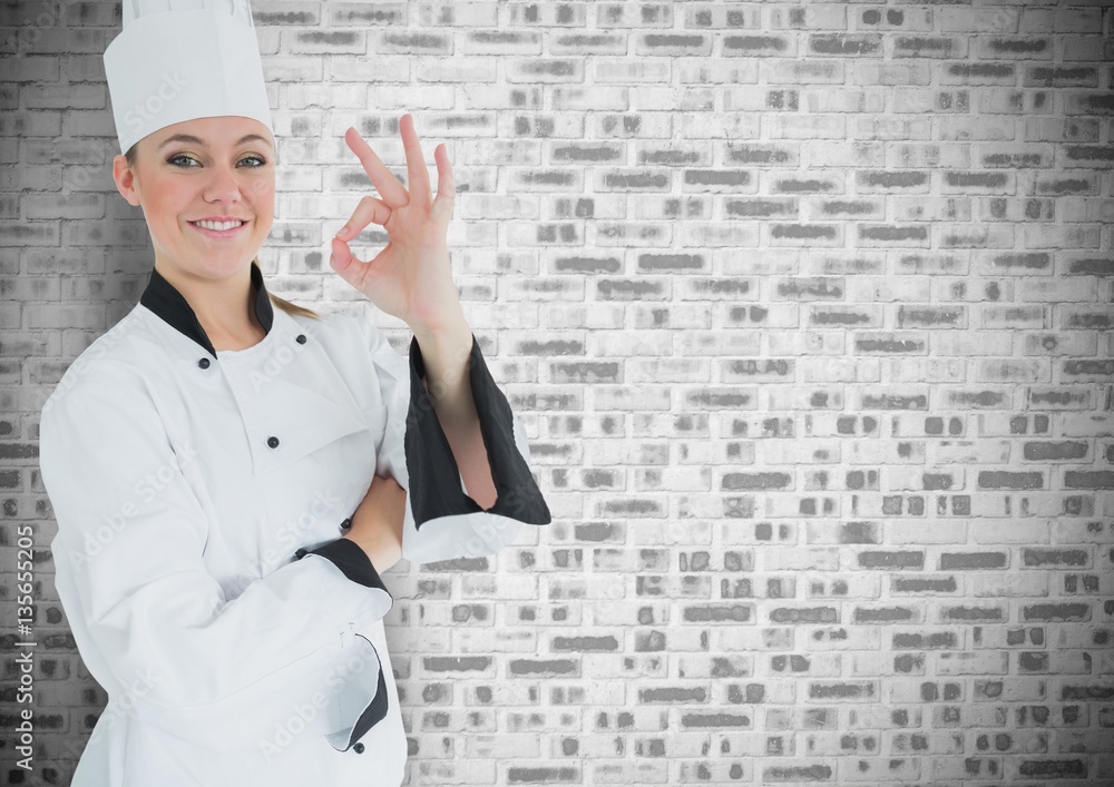 Happy female chef showing ok sign against brick wall