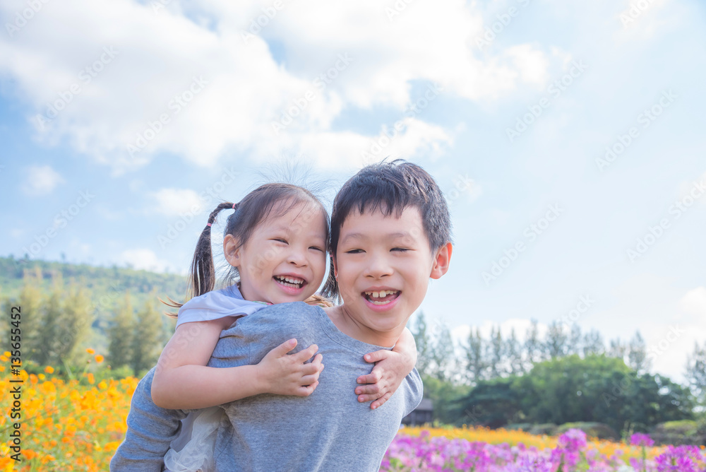 Asian brother holding his sister on his back and smiling togethe