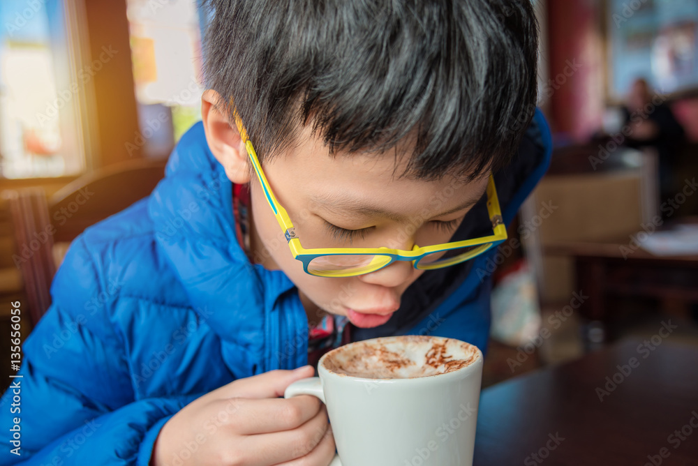 Young asian boy blowing hot chocolate drink in cafe