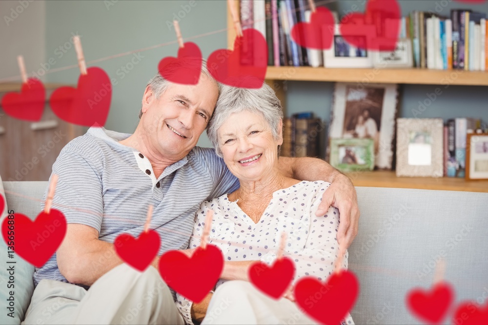 Composite image of red heart and senior couple embracing on sofa