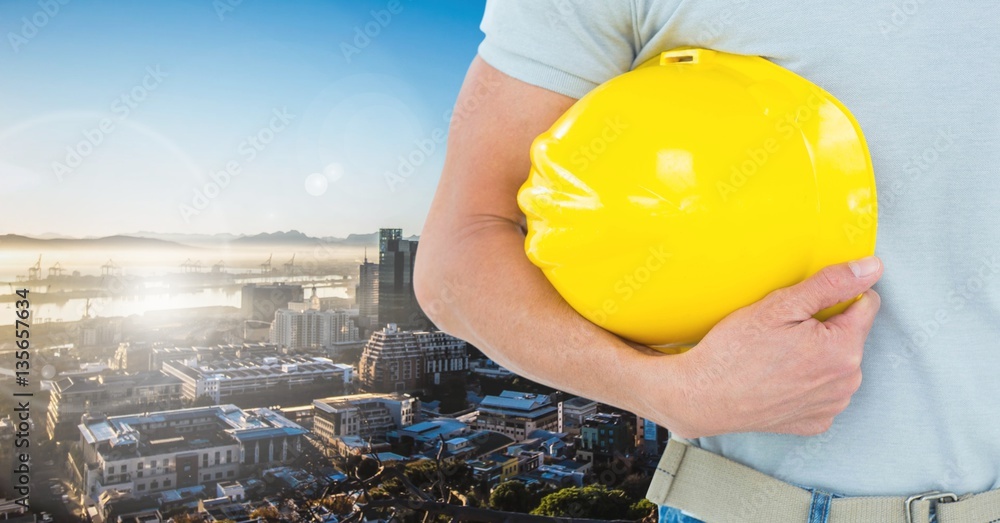 Handyman holding hard hat against cityscape