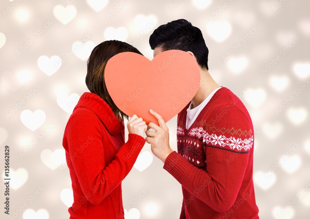 Romantic couple hiding their face behind red heart