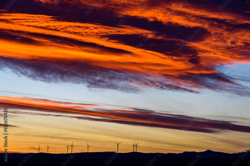 Wind Turbines Farm In The Distance On Beautiful Red, Orange And Blue Sunset