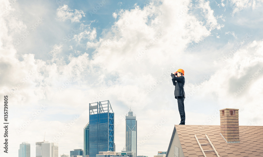 Engineer man standing on roof and looking in binoculars. Mixed m