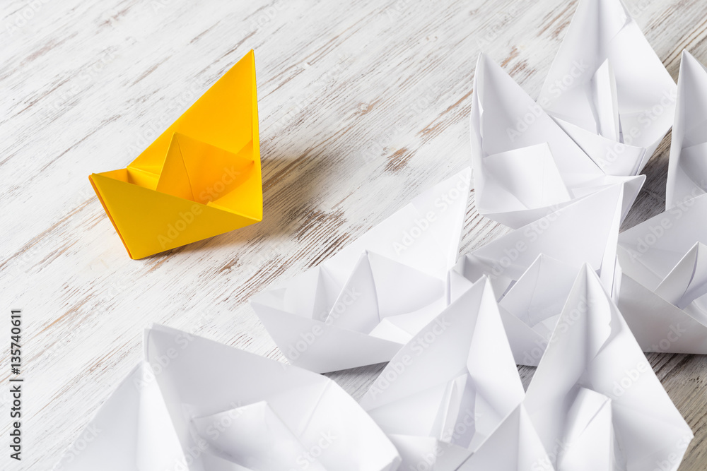 Business leadership concept with white and color paper boats on wooden table