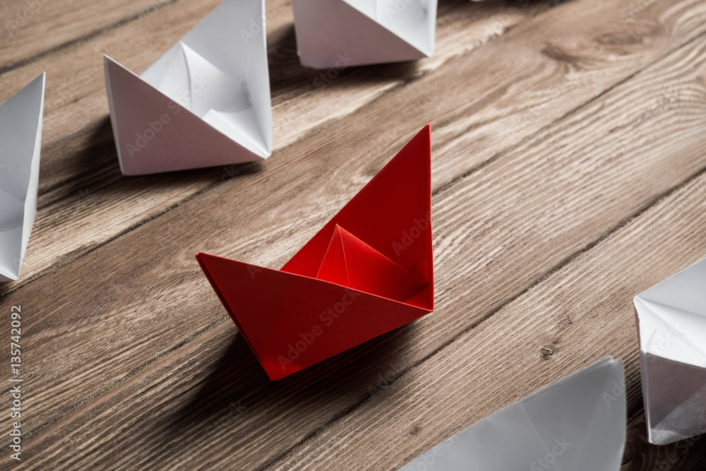 Business leadership concept with white and color paper boats on wooden table