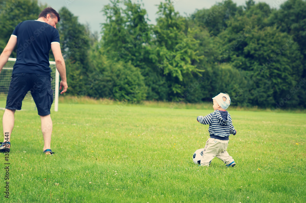 Little boy playing football on the field with gates