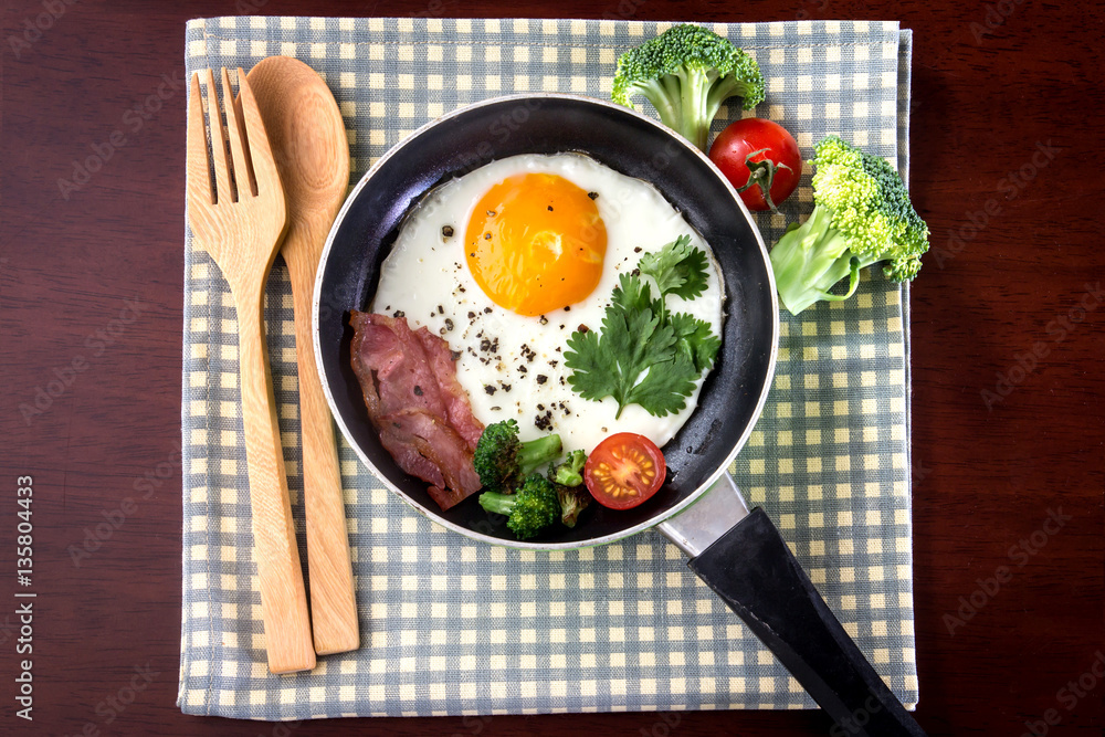 Breakfast with fried egg and bacon in dark pan on the table