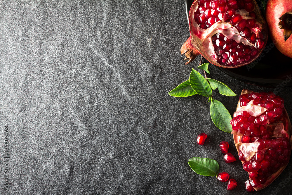 Fresh red pomegranate and seed  with leaves over black stone