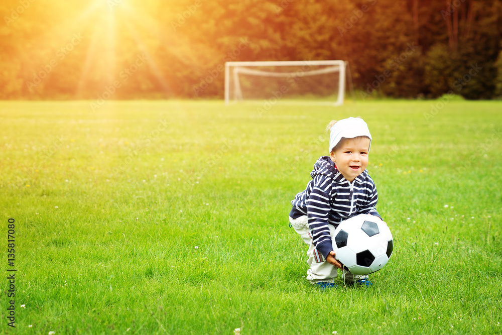 Little boy playing football on the field with gates